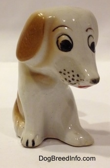 The front right side of a brown and white mixed breed puppy figurine in a sitting pose. The figurine has cartoon-y features.