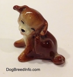 A figurine of a brown with white puppy scratching its neck.