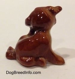 The right side of a figurine of a brown and white puppy that is scratching its neck. The figurine is glossy.