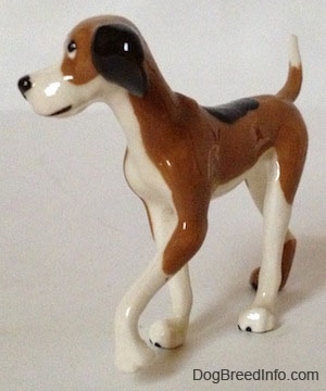 The front left side of a figurine of a tri-color Papa Dog. The figurine has a large black circle on its back.