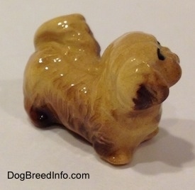 The front right side of a figurine of a brown and tan Pekingese puppy. The figurine is looking up and to the right.