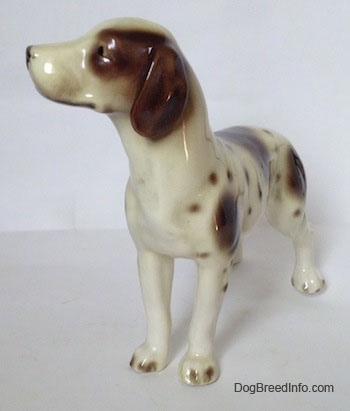 The front left side of a white and tan figurine of a Pointer with brown patches. The figurine has long brown ears.