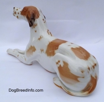 The back left side of a porcelain white with brown Pointer in a lying pose figurine. The tips of the figurines ears are black.