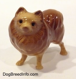 A figurine of a brown with tan standing figurine of a Pomeranian. The Figurine has black circles for eyes.
