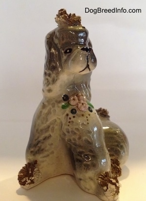 A ceramic spaghetti Poodle figurine. The figurine hhas flowers on it and it is in a sitting position.