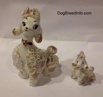 Two white spaghetti Poodle porcelain figurines that are in sitting positions. The bottoms of there ears are gold.