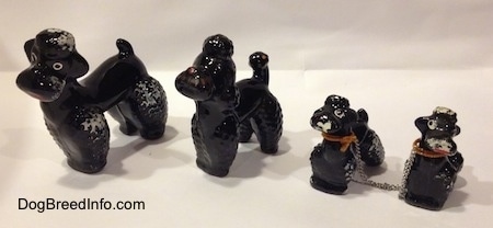 The front left side of four black clay Poodle figurines. Three of the figurines are chipped.