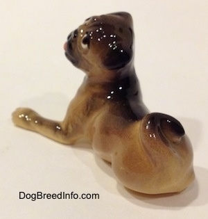 The back left side of a figurine of a brown with black miniature Pug lying down. The figurine has its tail swirled onto its back.