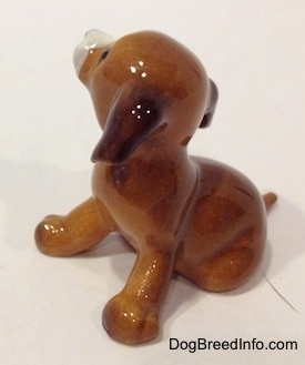 The left side of a figurine of a brown with white miniature puppy sitting figurine. The figurine has long ears.