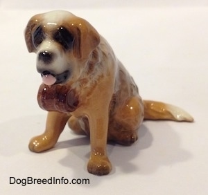 The front left side of a brown with white figurine of a Saint Bernard. The figurine has a barrel on its colllar.