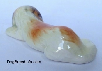 The back left side of a white with brown and black figurine of a Saint Bernard puppy in a lying position. It is hard to differentiate the tail of the figurine from the body of it.