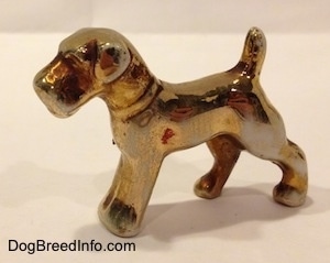 The front left side of a bone china figurine of a Schnauzer painted in gold. The figurine has small flopped over ears.