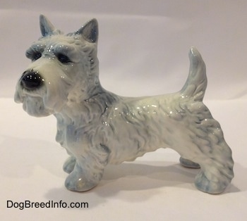 The left side of a white Scottish Terrier figurine with blue highlights. The figurine has short legs.