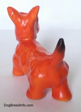The back left side of a figurine of an orange with black Scottish Terrier. The figurine has a black tipped tail.