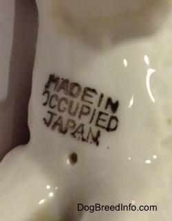 Close up - The underside of a porcelain figurine of a Standard Schnauzer figurine. The figurine has a stamp that reads 'Made in Occupied Japan'.
