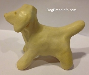The left side of a ceramic white dog the has a medium sized tail and it is arched up.