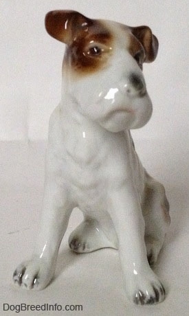 A figurine of a white with brown Wire Fox Terrier sitting figurine. The ears of the figurine are flopped over.