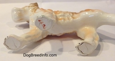 The underside of a white and tan figurine of a Wire Fox Terrier. The figurine has red numbers that read '7038' stamped on its front right leg.