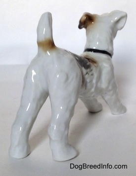 The back right side of a white with black and brown figurine of a Wire Fox Terrier. The figurine has its tail in the air.