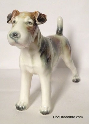 The front left side of a white with brown and black figurine of a Wire Fox Terrier. The figurine has small detailed eyes.