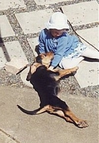 Misty the Bloodhound puppy laying outside next to a little girl who is wearing a white hat