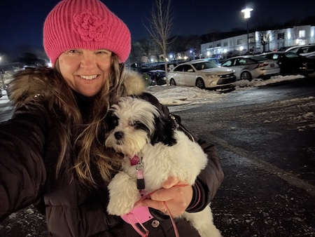 A girl wearing a pink hat holding a little fluffy white and black puppy outside in the winter time