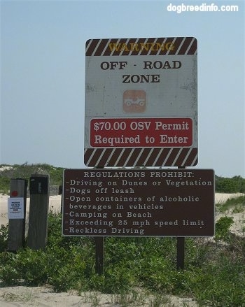 The sign says 'Warning Off-Road Zone $70.00OSV Permit Required to Enter' and another sign says 'REGULATIONS PROHIBIT: Driving on Dunes or Vegetation, Dogs off leash, Open containers of alcoholic beverages in vehicles, Camping on Beach, Exceeding 25mph speed limit, Reckless Driving'