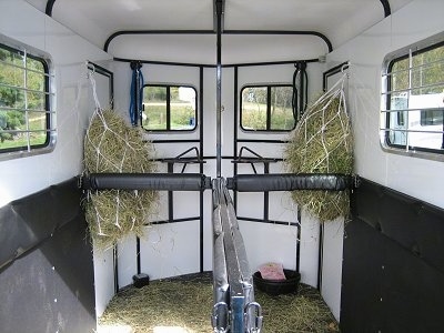 The inside of an empty trailer. There is green hay hanging up on the sides of a the trailer.