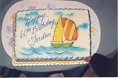 Annie the Black Lab is licking the frosting on a cake that says Happy 60th Birthday Gordon with a sailboat on it