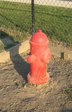 A Fake Fire Hydrant is in the corner of a dirt area.