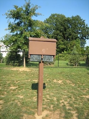 A wooden waste bag dispenser that is in a field.