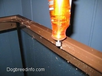 A dremel is being used on the back of the tank to cut into the brown plastic ledge. There is a blue wall in the background