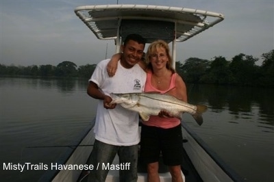 A man and woman are standing on a boat holding a snook fish. The lady has her arm wrapped around the man.