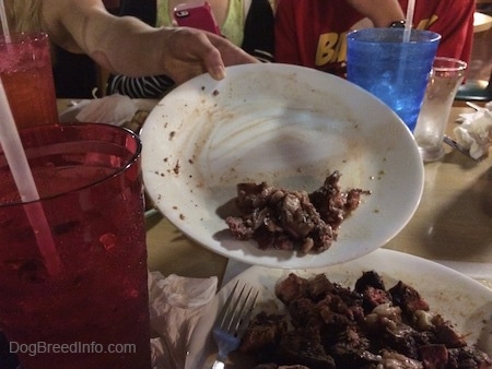 A white plate a third full of steak being dumped onto a larger plate full of steak