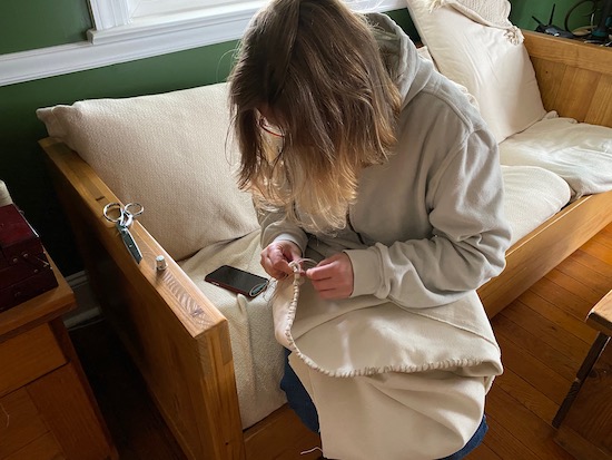 A lady sitting on a couch sewing an all natural dog bed by hand