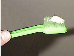 Close up - A person holding a green toothbrush with toothpaste on it.