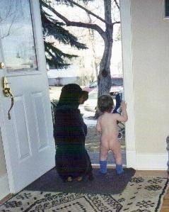 A black with brown Rottweiler is sitting in a doorway next to a naked baby who is only wearing purple socks.