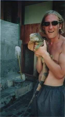 A shirtless man is holding a huge iguana.