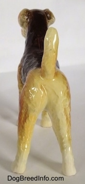 The back of a black and tan with white Vintage Goebel Airedale Terrier porcelain dog figurine. The dogs legs are straight and its tail is up.