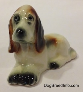 The front left side of a white with black and red Basset Hound figurine. The figurine has very detailed eyes.