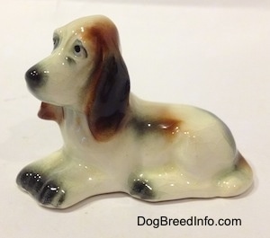 The left side of a white with black and red Basset Hound figurine. The figurine is glossy.