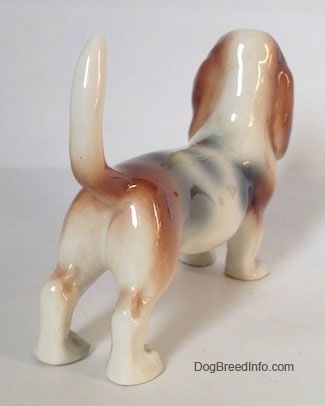 The back right side of a white with black and red Basset Hound figurine.