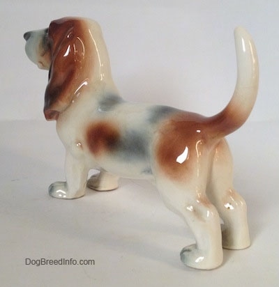 The back left side of a white with black and red Basset Hound figurine. There are shaping details on the ear of the figurine.