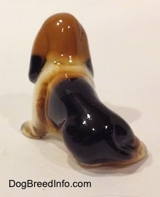 The back left side of a black, brown and white ceramic Basset Hound figurine. The figurine is very glossy.