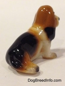 The back right side of a black, brown and white ceramic Basset Hound figurine. The figurine lacks fine detail.