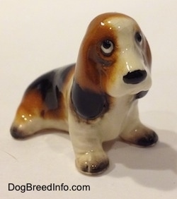 The front left side of a black, brown and white ceramic Basset Hound figurine. The figurine eyes lack fine details.