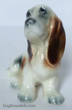 A white with black and red ceramic Basset Hound figurine. The figurine is looking up and to the left.