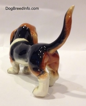 The back left side of a black with white and brown Basset Hound figurine. The figurine has fine detail.