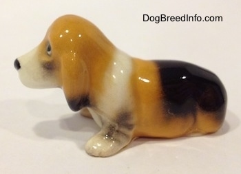 The left side of a tan and black with white ceramic Basset Hound figurine. The ears of the figurine is detailed.
