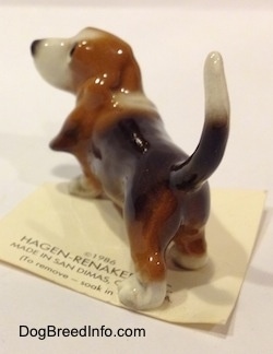 The back left side of a black and brown with white Basset Hound figurine. The figurines tail is arched up.